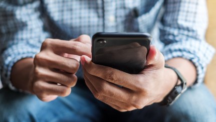 Image shows a man’s hands holding a cell phone.