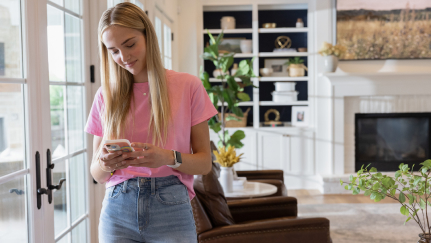 Young woman standing indoors looking at a mobile phone.